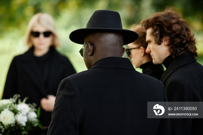 Back view of man wearing black standing at outdoor funeral ceremony with group of people