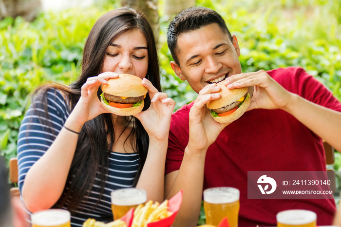 Happy couple eating hamburgers and drinking ice cold beers