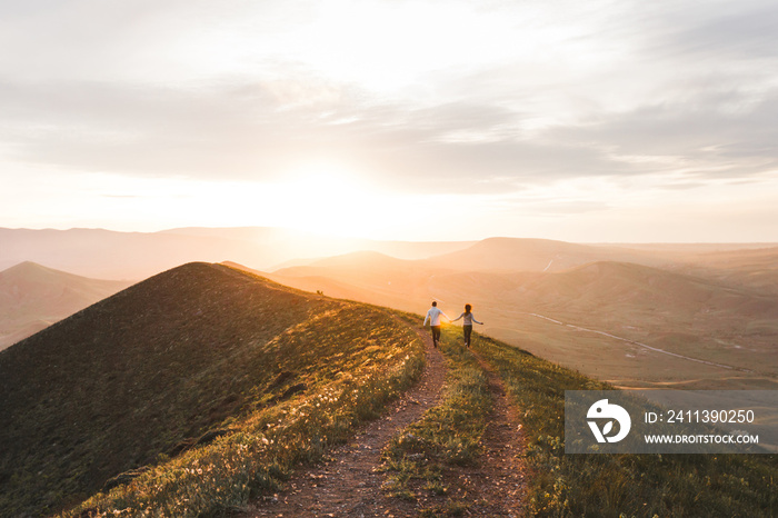 Young couple running together by sunset hill with amazing mountain view