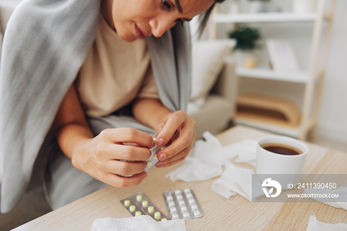 A woman with a cold with pills is treated at home chooses which drugs to take and self-medicates, checks the expiration date while sitting on the couch at home