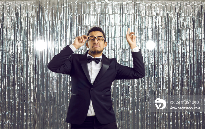 Overjoyed young African American man entertainer in formal suit and glasses dance on glitter disco background. Smiling black male mc or discoman have fun in club. Entertainment concept.