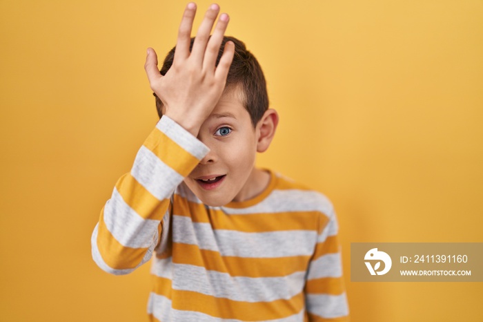 Young caucasian kid standing over yellow background surprised with hand on head for mistake, remember error. forgot, bad memory concept.