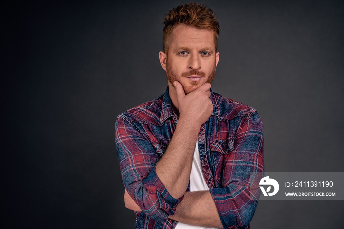 Good-looking smart businessman hearing out interesting concept of employer, liking new fresh idea, rubbing beard with hand and staring thoutghtful at camera while thinking or making own opinion