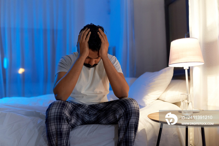 sleeping problem, bedtime and insomnia concept - stressed indian man sitting on bed at night at home