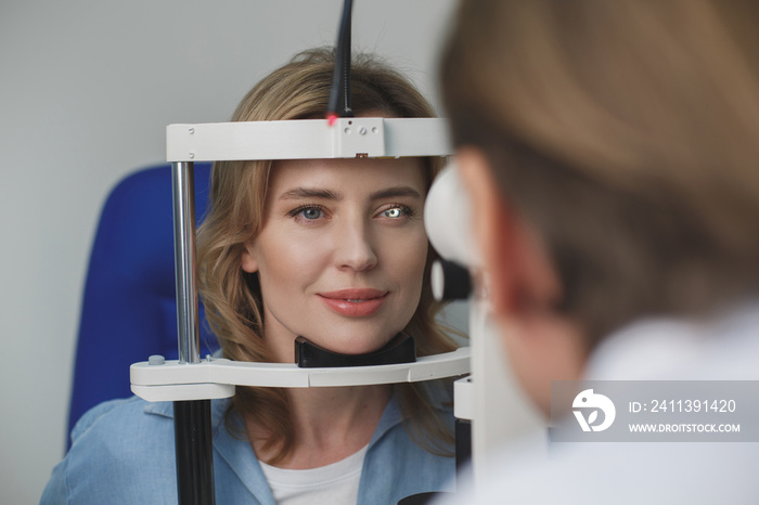 Portrait of smiling female client checking eyesight with equipment opposite doctor. Ophthalmology concept