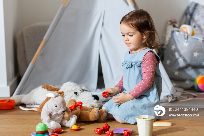 childhood, leisure and people concept - happy little baby girl playing with tea party game soft toys at home