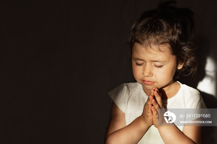 A little girl folded her hands in prayer in the hope of ending the war in Ukraine, a Ukrainian child prays and believes in a happy future