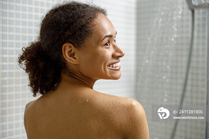 Close up of smiling african woman taking a shower in bathroom. Spa, wellness and relaxation concept