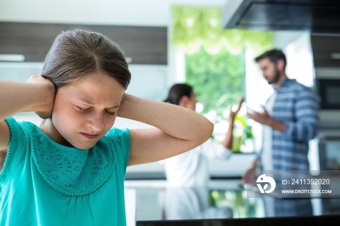 Sad girl covering her ears while parents arguing in background