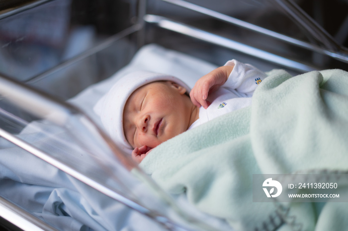 Close up portrait of adorable little newborn baby girl lying quiet at hospital crib hours after coming to life