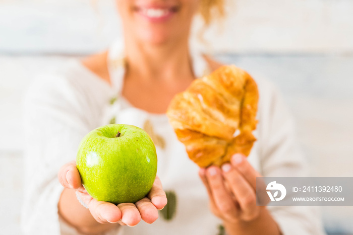 close up of beautiful woman holding an apple and croissant in front of the camera choosing between a healthy life of unhealthy lifestyle - dieting and taking care of the food