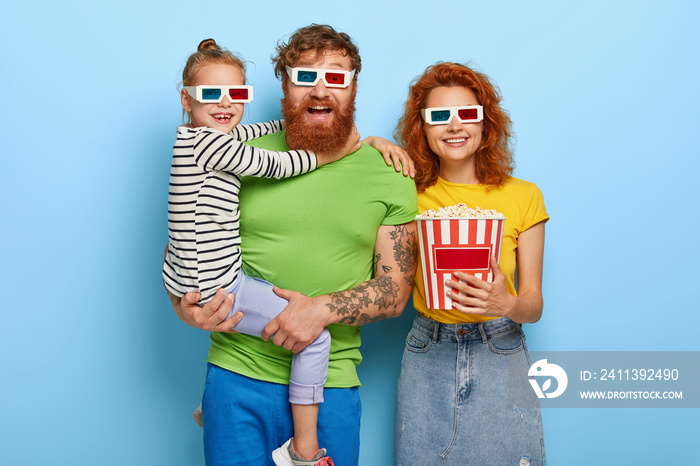 Happy family enjoy film or cartoon in cinema, wear 3d glasses, amused by cool sound and visual effects, eat delicious snack. Small girl on fathers hands, embraces him. People, leisure, weekend