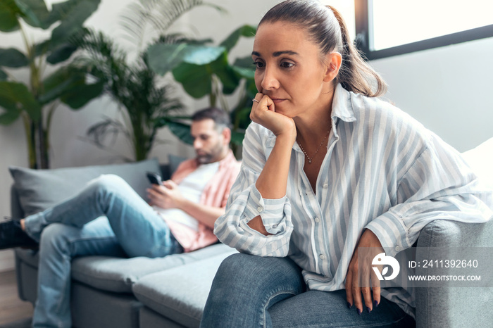 Angry young couple sitting on couch together and looking to opposite sides at home.