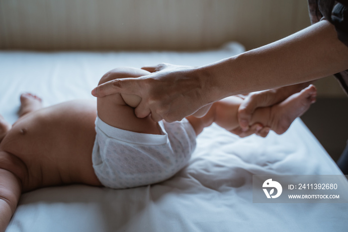 mother holds the feet of a baby child lying in bed giving massage