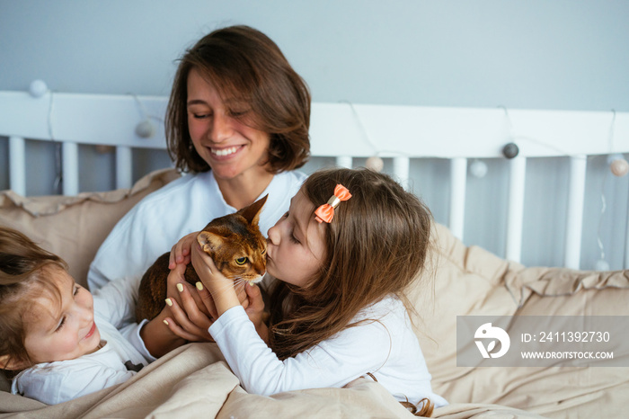 Happy mother and two daughters smiling hugs in bed