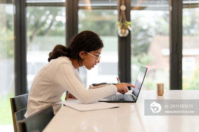 Girl doing homework and using laptop in living room