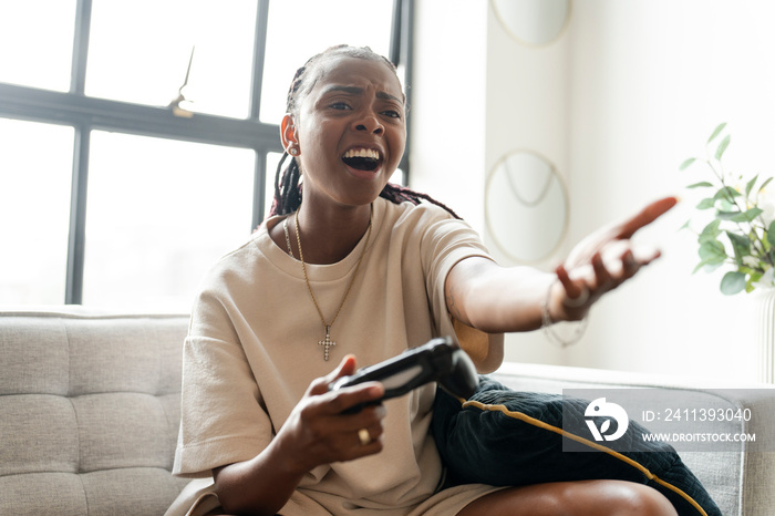 Disappointed young woman playing video games while sitting on sofa at home