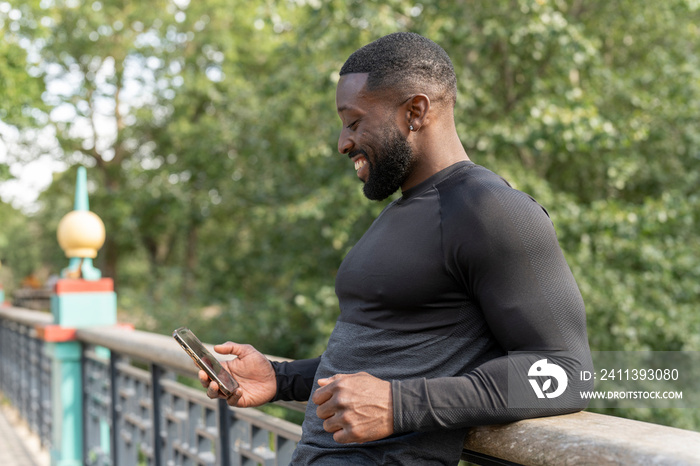 Smiling athletic man looking at smart phone on footbridge in park