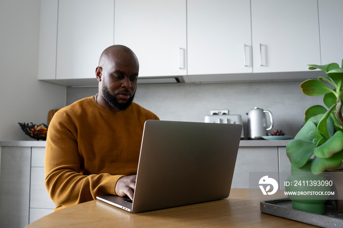 Man using laptop at table in kitchen