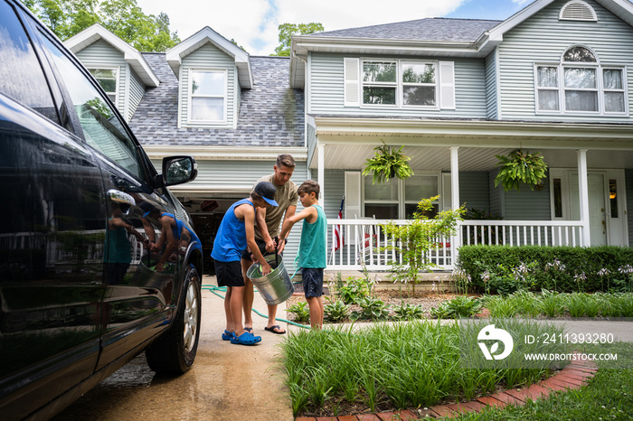 Air Force service member washes his vehicles with his sons in the driveway.