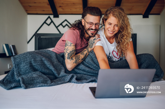 Romantic couple lying in the bed at home in the morning and using laptop