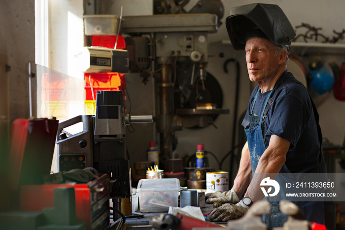 Senior man looking away while standing by workbench in workshop