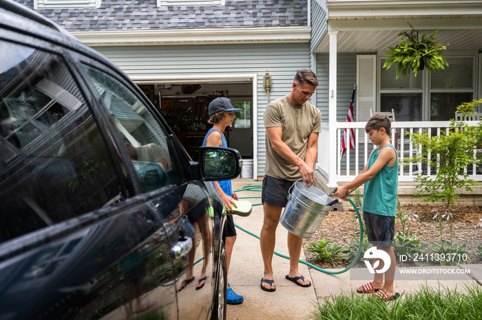 Air Force service member washes his vehicles with his sons in the driveway.