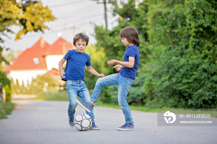 Two cute little kids, playing football together, summertime. Children playing soccer