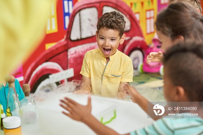 Emotional kid watching chemical experiment in playroom. Happy kids having fun in entertainment center. Birthday party celebration.