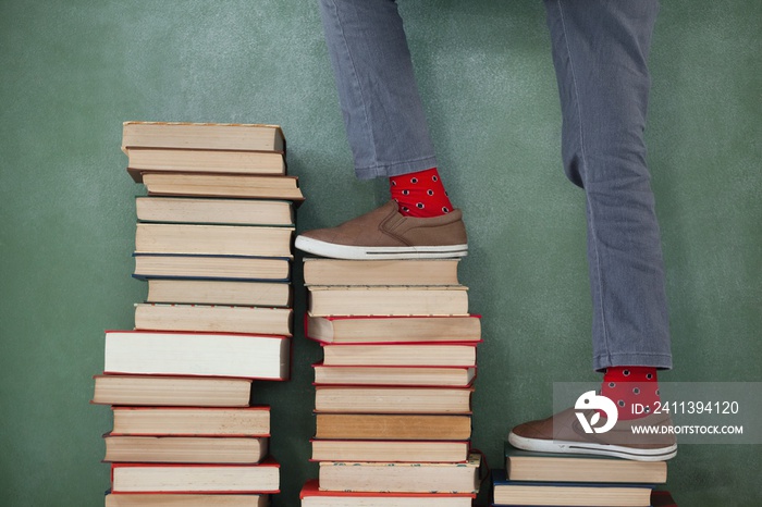 Schoolboy climbing steps of books stack against chalkboard