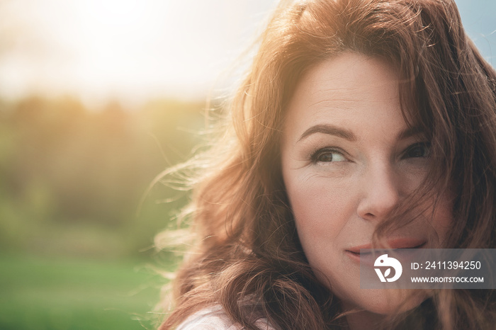 Natural beauty. Close up portrait of dreamful woman with red curly hair. She is looking aside with enjoyment and smiling while resting in the fresh air. Copy space