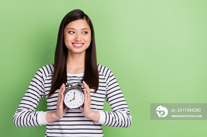 Portrait of attractive minded cheerful girl holding in hands clock thinking copy space isolated over green color background