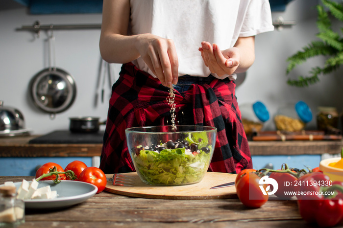 young girl prepares a vegetarian salad in the kitchen, she salts and adds spices, the process of preparing healthy food