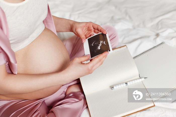 Pregnant woman sitting on bed and writing in notebook