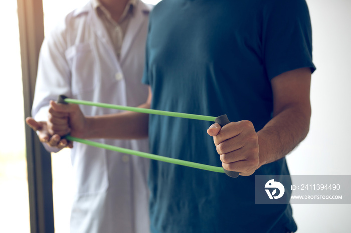 Patient doing stretching exercise with a flexible exercise band and a physical therapist hand to help in clinic room.