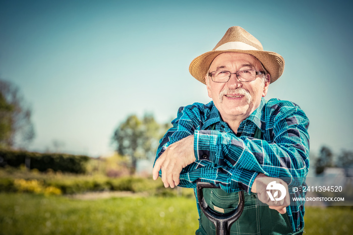 Portrait of a senior gardener standing in a garden with a shovel.