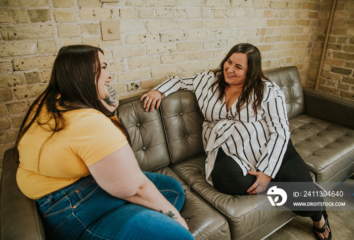 2 plus size metis women sit on sofa smiling