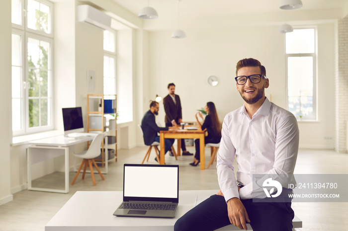 Young businessman sitting on desk with laptop with empty screen in company office