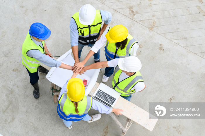 Top view of contractors, engineers and formats team in vests with helmets working with laptops on under-construction site. Home building project. Engineer foreman discusses with coworker at workplace