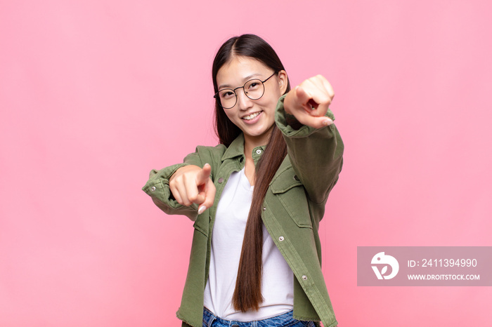 asian young woman feeling happy and confident, pointing to camera with both hands and laughing, choosing you