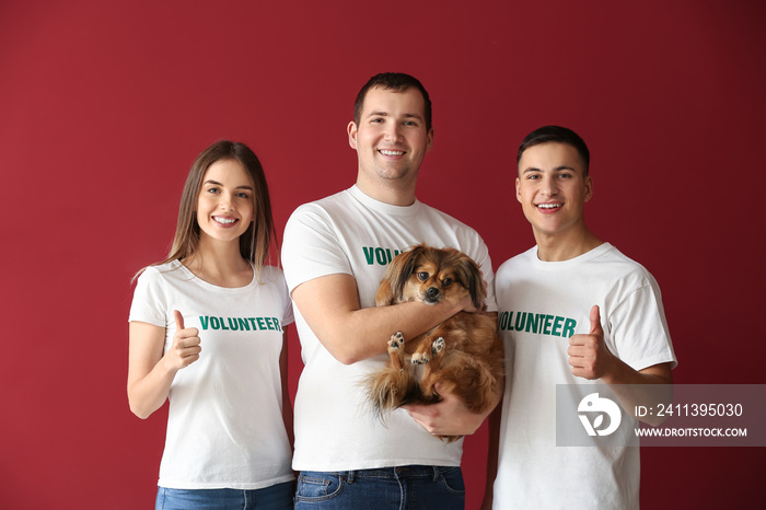 Young volunteers with dog on color background