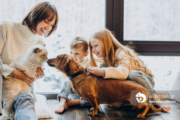 Mother with son and daughter playing with their dog at home by the window