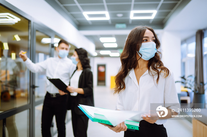 Portrait of young business woman in protective face mask an office building hallway. Office worker working during pandemic in quarantine city. COVID - 19.