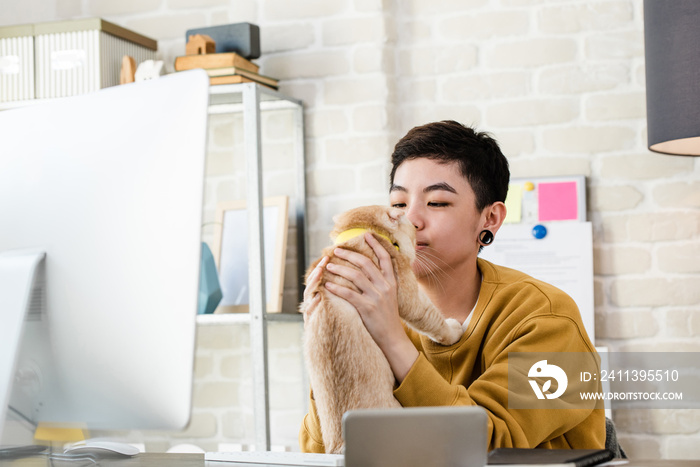 Young Asian tomboy woman in casual attire  holding her cat during working from home in living room