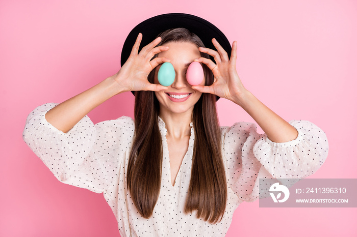 Photo of adorable funny young woman dressed white clothes cap easter eggs cover eyes isolated pink color background