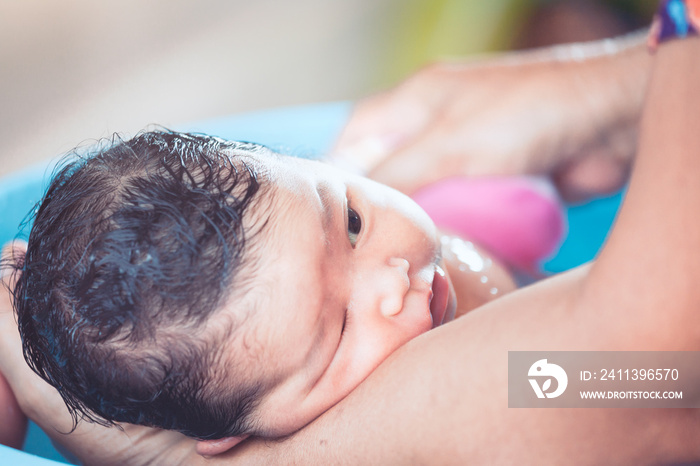 Cute asian newborn baby girl take a bath in bathtub. Mom cleaning her baby body with tenderness