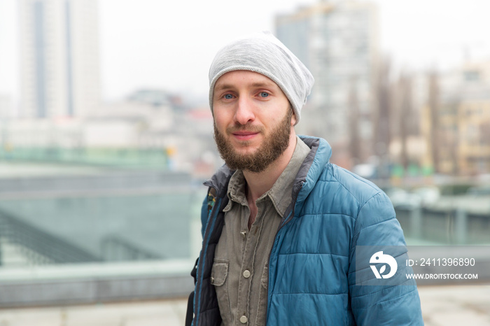 Portrait of a young man with a jacket and hat on a background of the city.