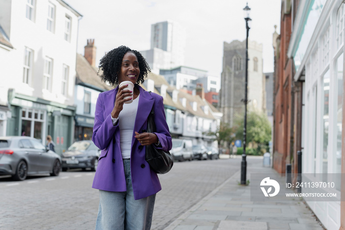 Smiling woman walking and drinking coffee on sidewalk