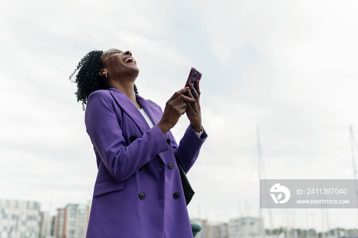 Woman laughing while using smart phone in city