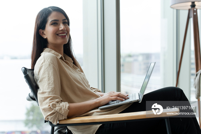 Businesswoman with laptop sitting in office lobby